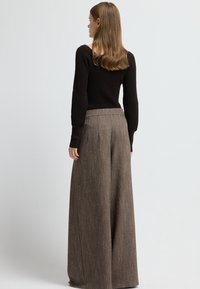 Pantaloni larghi marroni con un motivo testurizzato e sottili righe verticali, abbinati a un maglione a coste neri aderente, visti da dietro.