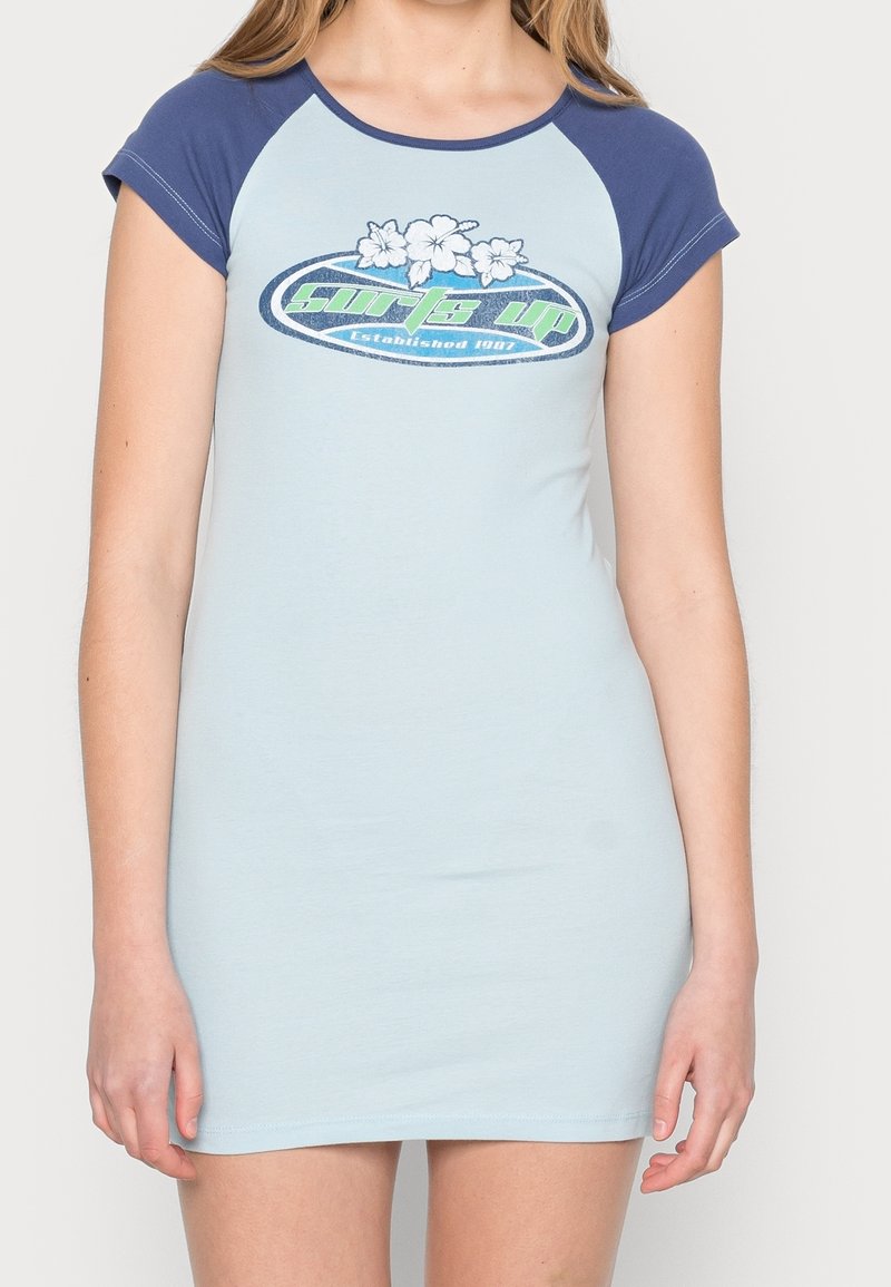 Světle modré šaty s krátkými tmavě modrými rukávy, s grafickým designem květin a nápisem "Surf's Up Established 1907" vepředu.