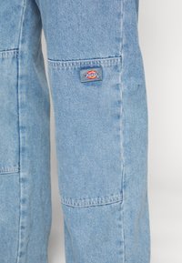 Lyseblå denimbukser med et merkeplaster, synlige sømmer og en løs passform.
