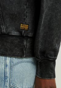 Felpa in denim nero con polsini e orlo a costine, dotata di un'etichetta dorata G-Star Originals. Jeans azzurri con design classico della tasca posteriore.