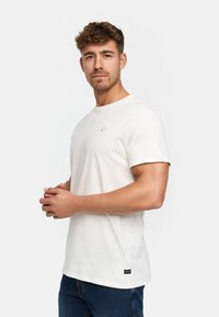 Weißes Baumwoll-T-Shirt mit kurzen Ärmeln, Rundhalsausschnitt, kleinem Logo-Detail auf der Brust und geradem Saum, kombiniert mit blauen Jeans.