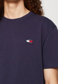 Marinblå bomullströja med rund hals och korta ärmar. Litet rektangulärt "TOMMY JEANS"-märke i rött, vitt och blått på bröstet.