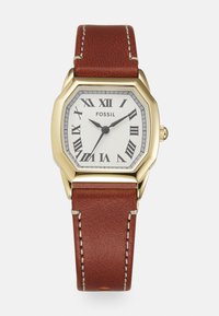 Montre octogonale en acier inoxydable doré avec un cadran texturé blanc, des chiffres romains et un bracelet en cuir brun avec des coutures blanches.