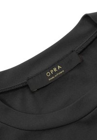 Czarny t-shirt z naszywką o gładkiej fakturze. Na wewnętrznej stronie widoczna etykieta z napisem "OPRA" w złotym kolorze, informująca "Wyprodukowano w Polsce".