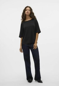 Camiseta negra de gran tamaño con mangas anchas, combinada con jeans de campana azul oscuro y zapatos negros de punta. Textura suave, ajuste casual.