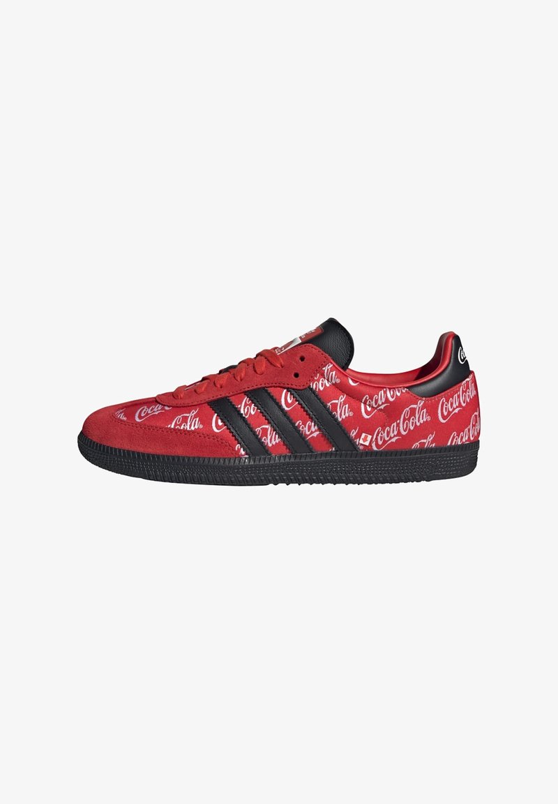Baskets rouges Adidas avec des bandes noires et une semelle noire, avec des logos Coca-Cola blancs partout sur la tige en tissu.