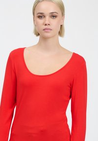 Rotes Langarmoberteil mit weitem Rundhalsausschnitt, aus weichem Stoff gefertigt. Verfügt über eine figurbetonte Passform und glatte Textur, ohne Muster oder Verzierungen.