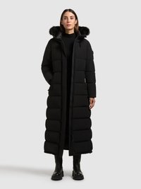 Čierny dlhý puffový kabát s kapucňou lemovanou umelej kožušiny, prešívaným dizajnom, predným zipsom a bočnými vreckami. Skombinovaný s čiernymi čižmami po kolená.