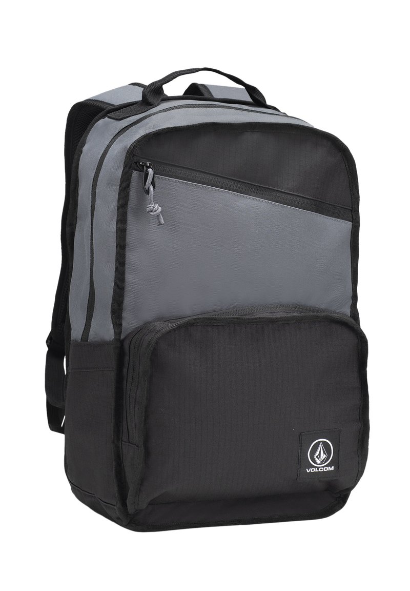 Mochila gris y negra hecha de un tejido duradero, que cuenta con múltiples compartimentos con cremallera, un asa superior y un parche con el logo en la parte frontal.
