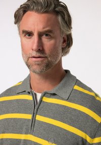 Grå pikétröja med gula horisontella ränder, tillverkad av mjukt stickat material. Har en krage och en delvis framzipper.