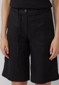 Schwarze Leinen-Shorts mit gebundenem Bund, seitlichen Taschen und lockerer Passform, die knapp oberhalb des Knies endet und einen sauberen Saum hat.