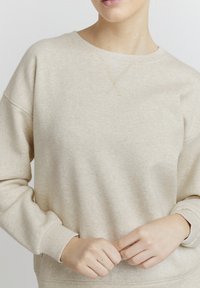Beige genser med rund hals, ribbestrikkede mansjetter og en myk tekstur. Merkbar sømdetalj i en lysere nyanse over brystet.