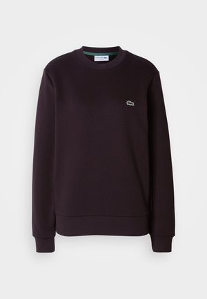 Tumevioletne pusakamps pehmest kangast, kraega, soonikkoes varrukate ja väikese rohelise Lacoste'i logoga rinnal.