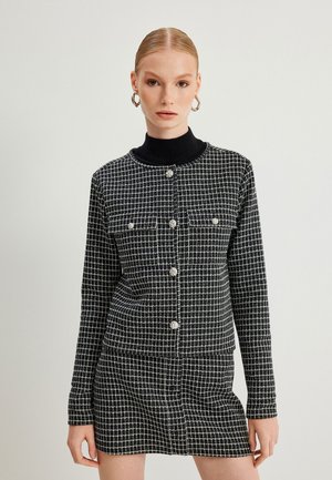 Veste à carreaux noir et blanc avec manches longues, fermeture à boutons sur le devant, deux poches et jupe mini assortie, au design en tissu texturé.