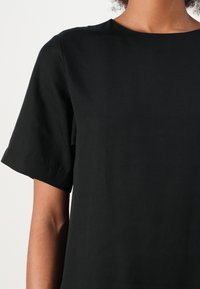 Black short-sleeve top with a round neckline, made of smooth fabric. Visible stitching on the sleeves, no patterns or accents.