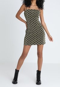 Svart prickig klänning med en åtsittande form, tillverkad av strukturerad tyg, med tunna band och en nederkant ovanför knäet. Buren med svarta boots.