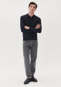 Tengerészkék hosszúujjú póló, galléros nyakkal és három gombbal, szürke farmernadrággal és fekete slip-on cipőkkel párosítva. Egyszerű dizájn, testhezálló szabás.