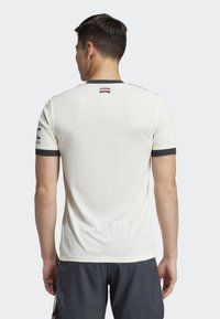 Lys beige treningsskjorte med korte ermer, teksturert stoff, grå detaljer på ermene, og logo ved baksiden av nakken.