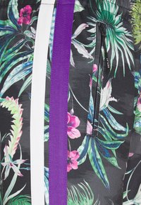 Blommiga badshorts i svart tyg med gröna och rosa tropiska mönster. Detaljer inkluderar vita och lila ränder samt en ficka med dragkedja.