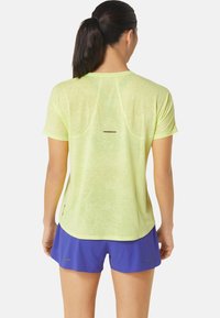 Jasnozielona, sportowa koszulka z krótkim rękawem, o fakturowanym wykończeniu i refleksyjnym akcentem. W zestawie z niebieskimi sportowymi szortami.