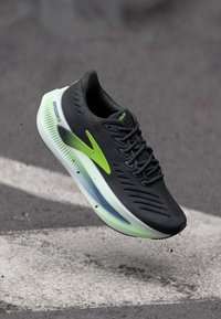 Czarny but do biegania z fakturowaną cholewką, zielonymi akcentami i półprzezroczystą podeszwą; zaprojektowany z myślą o wydajności i stabilności.