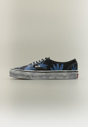 Baskets Vans noires avec un motif de feuilles tropicales bleues, lacets blancs et semelle en caoutchouc blanche au look usé et vieilli.