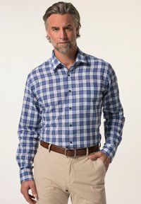 Camisa a cuadros azul y blanca de botones con mangas largas, con cuello puntiagudo y botones negros, combinada con pantalones beige claros.