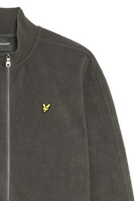 Fleecejacka i mörkgrått med hög krage och en silverfärgad dragkedja. Har en liten broderad logotyp i gult på vänster bröst.