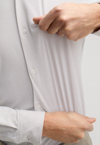 Camicia bianca a maniche lunghe con motivo a quadri e texture liscia. Bottoni visibili al centro e ai polsini.