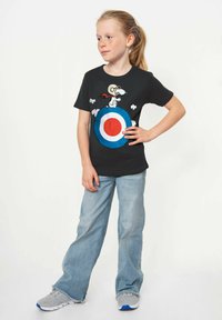 Black short-sleeve T-shirt featuring a graphic of Snoopy on a target with red, white, and blue colors. Paired with light blue jeans and gray sneakers.