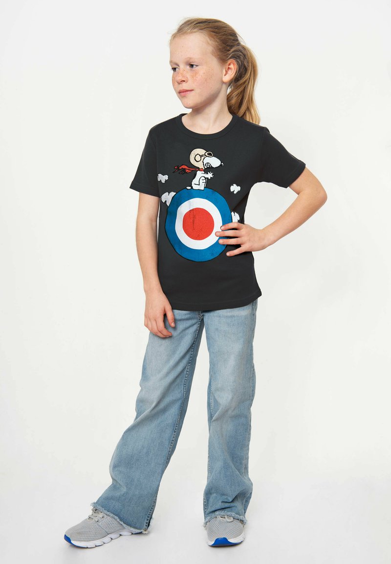 Black short-sleeve T-shirt featuring a graphic of Snoopy on a target with red, white, and blue colors. Paired with light blue jeans and gray sneakers.