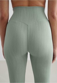 High-waisted leggings in soft green fabric with vertical ribbed texture. Seam details accentuate the contour at the back.