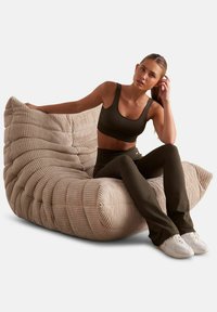 Chaise lounge en velours côtelé beige avec un design ondulé unique et une texture douce ; présente des bords arrondis et un profil bas pour un salon décontracté.