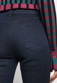 Jeans de mezclilla azul oscuro con un diseño ajustado, que cuentan con dos bolsillos traseros y detalles de costura sutiles. Tejido texturizado y cintura de altura media.