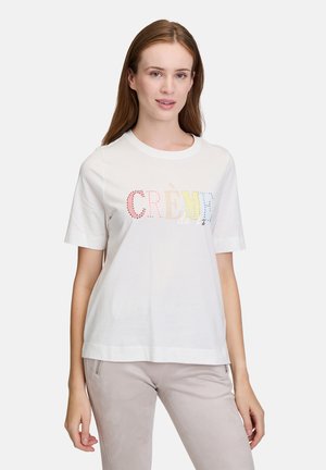 T-shirt en coton blanc à manches courtes et col rond. Présente un texte "CRÈME de la" dégradé en couleurs pastel, agrémenté de strass.