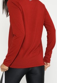 Camicia rossa a maniche lunghe con un design testurizzato e perforato sul retro; presenta un piccolo logo all'altezza del collo e una forma attillata.