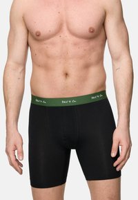 Schwarze Boxer-Shorts aus weichem Material, mit enger Passform und einem grünen Bund mit weißem Text. Nahtloses Design, mittellange Beine.