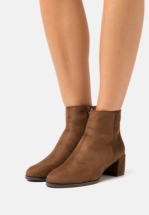 Bottines en daim marron avec un bout rond et un petit talon carré. Elles possèdent une fermeture éclair sur le côté pour un enfilage facile. Texture lisse et design épuré.