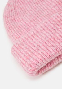 Rosa strikket lue med ribbestruktur, mykt materiale og brettkantdetalj. Stoffet har en lett pusefinish.