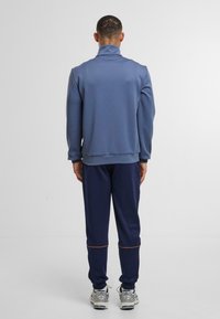 Námořnický modrý sportovní svetr s vysokým límcem, texturovaná látka a odpovídající námořnické tepláky s oranžovým akcentem na manžetách.