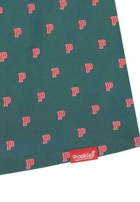 Zelená látka s opakujícím se červeným vzorem „P“, s červenou visačkou označenou „Pookies Couch Couture“ v pravém dolním rohu.