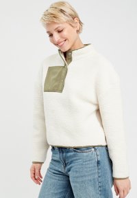 Fleece-Pullover in Creme mit olivgrünem Kragen und Patch; verfügt über Druckknöpfe, eine lockere Passform und eine strukturierte Oberfläche.
