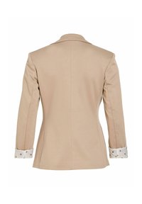 Blazer beige tailleur vu de dos avec des poignets blancs à pois marron.