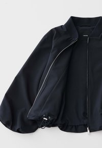 Black zip-up jacket with ribbed collar, adjustable drawstring hem, and long sleeves laid flat on white background.