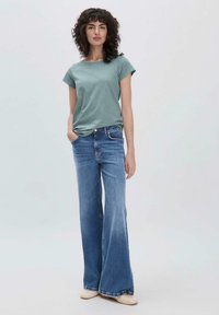 Camicetta verde menta a maniche corte abbinata a jeans a gamba larga blu chiaro, che mostrano un look casual e una texture morbida in un ambiente minimalista.