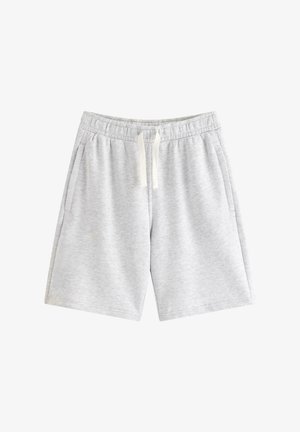 Dreng står iført en marineblå ærmeløs skjorte, lysegrå knælange shorts, hvide sokker og hvide sneakers på en ensfarvet baggrund.