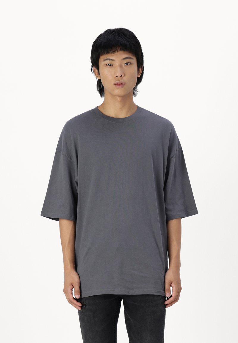 Mørk grå oversized t-skjorte i myk bomull, med rund hals og korte ermer, kombinert med svarte jeans. Glatt tekstur, minimalistisk design.