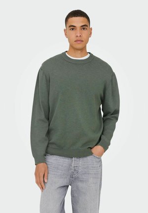 Groene gebreide trui met een ronde hals, lange mouwen en ribbels aan de mouwen. Draag over een wit shirt en gecombineerd met lichtgrijze denim jeans.