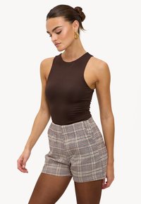 Body marron sans manches associé à un short taille haute à carreaux crème, rouge et noir. Texture lisse avec une coupe ajustée. Boucles d'oreilles créoles dorées.