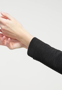 Černý ribbovaný látkový rukáv s texturovaným designem, těsně obepínající zápěstí, s hladkým vnitřním materiálem a čistými liniemi.